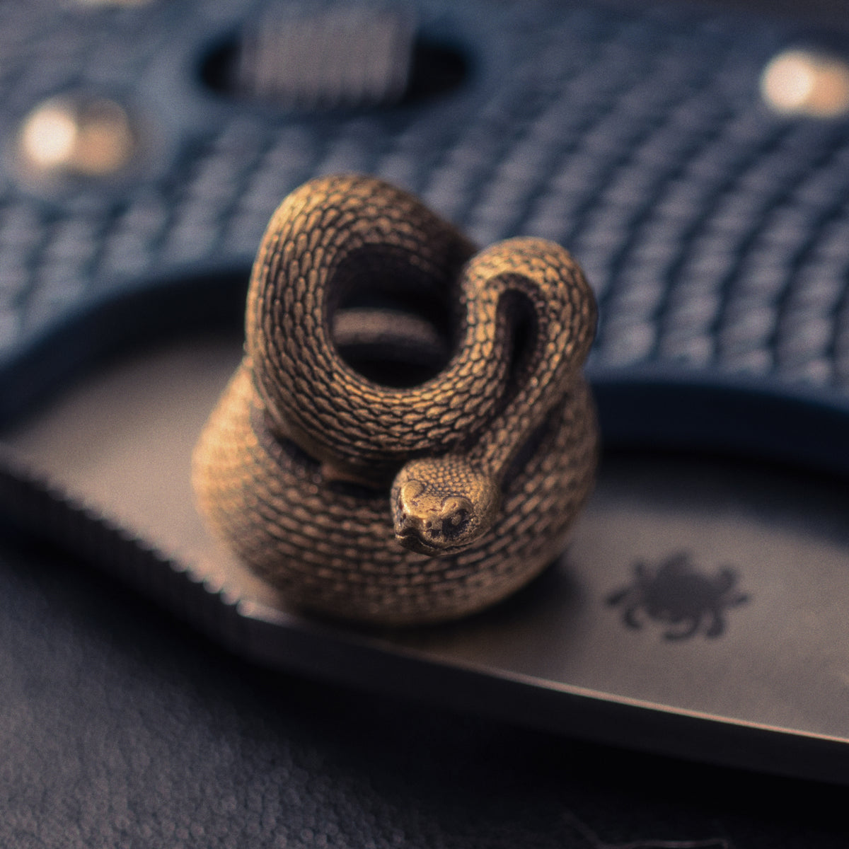 Rattlesnake paracord bead attached to an EDC knife lanyard, showing the sculpted snake head, coiled body and aged brass finish.
