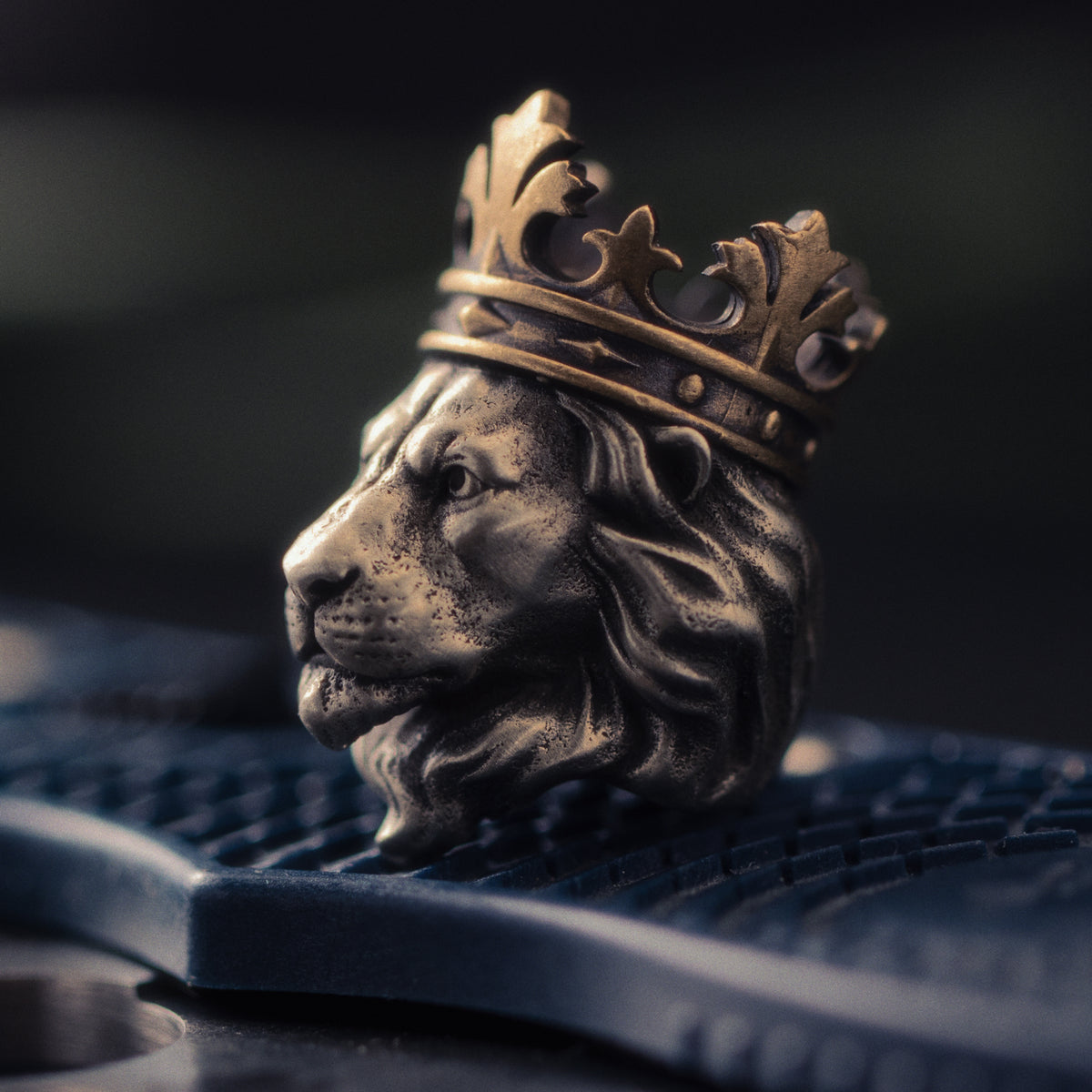 Macro close-up of the Lion King EDC bead showing the hand-aged lion face, layered mane, dark recessed details and brass crown.