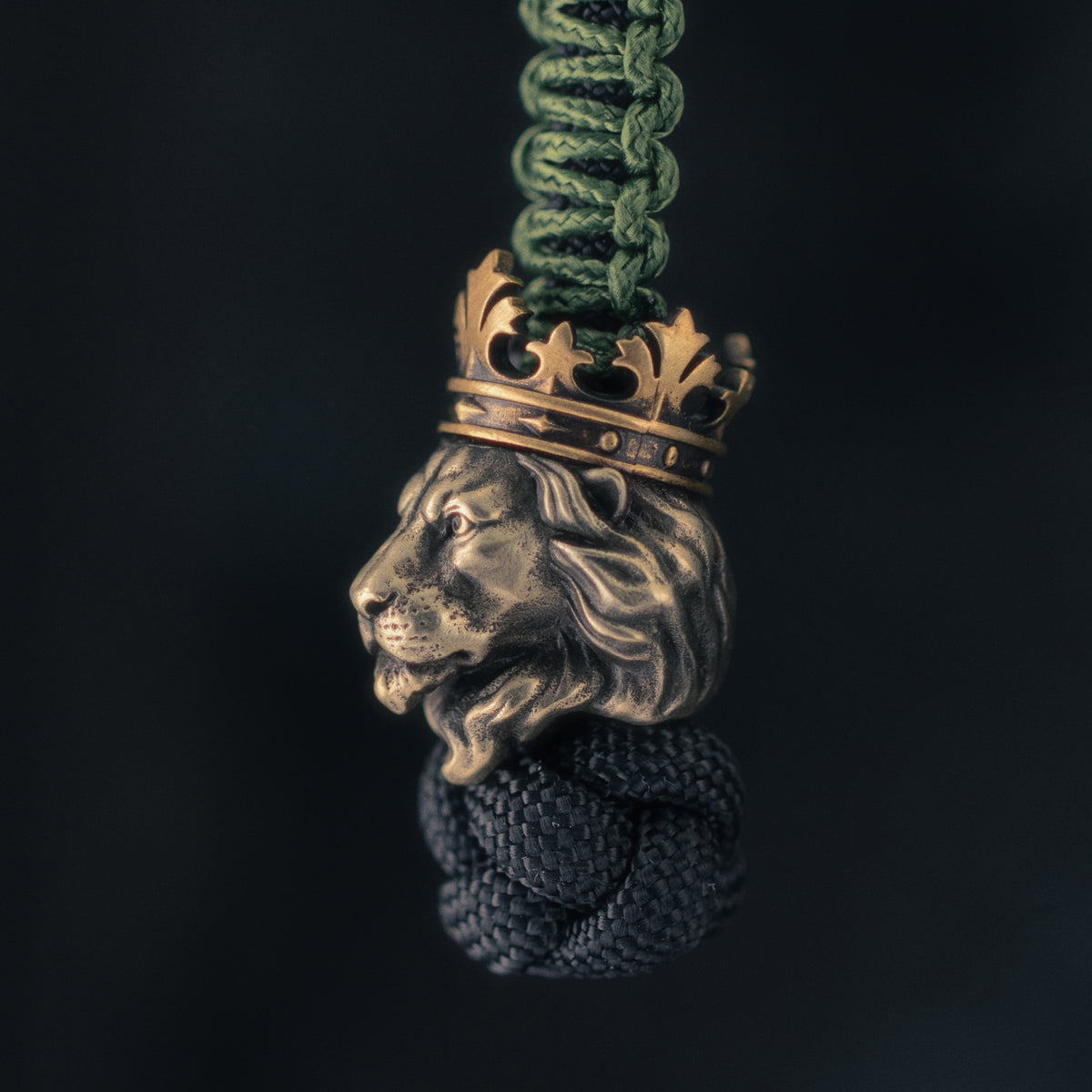Side view of a crowned lion EDC bead mounted on paracord, highlighting the sculpted muzzle, flowing mane and brass crown.
