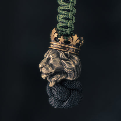 Side view of a crowned lion EDC bead mounted on paracord, highlighting the sculpted muzzle, flowing mane and brass crown.
