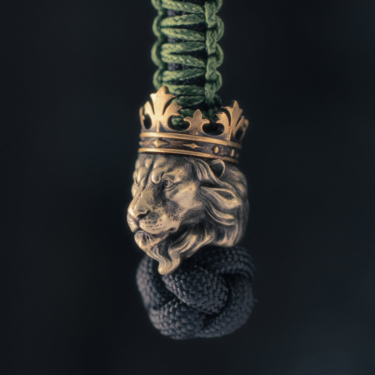 Three-quarter view of a Lion King knife lanyard bead showing the white brass lion head, strong facial structure and integrated brass crown.