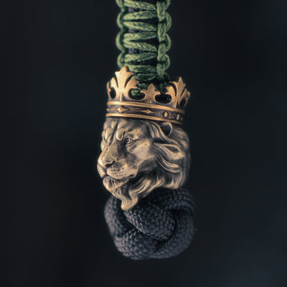 Three-quarter view of a Lion King knife lanyard bead showing the white brass lion head, strong facial structure and integrated brass crown.