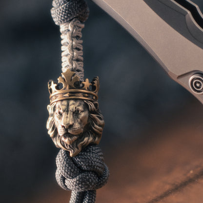 front view of a crowned lion EDC bead mounted on paracord, highlighting the sculpted muzzle, flowing mane and brass crown.