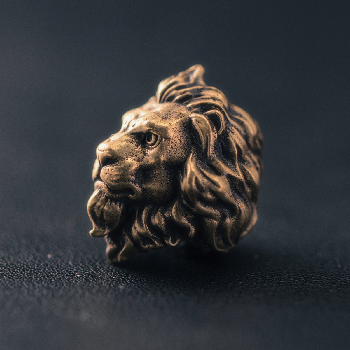 Side profile of a lion paracord bead showing the sculpted muzzle, layered mane and hand-finished aged metal texture.