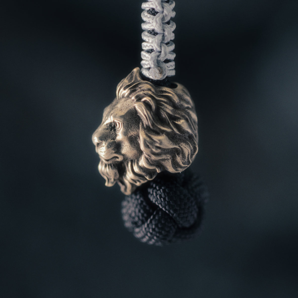 Side view of a lion knife lanyard bead mounted on paracord, showing the strong muzzle and layered mane sculpture.
