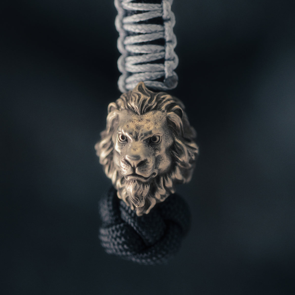 Front view of a brass lion head EDC bead attached to braided paracord with a detailed sculpted mane and aged finish.