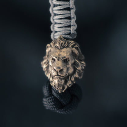 Front view of a brass lion head EDC bead attached to braided paracord with a detailed sculpted mane and aged finish.