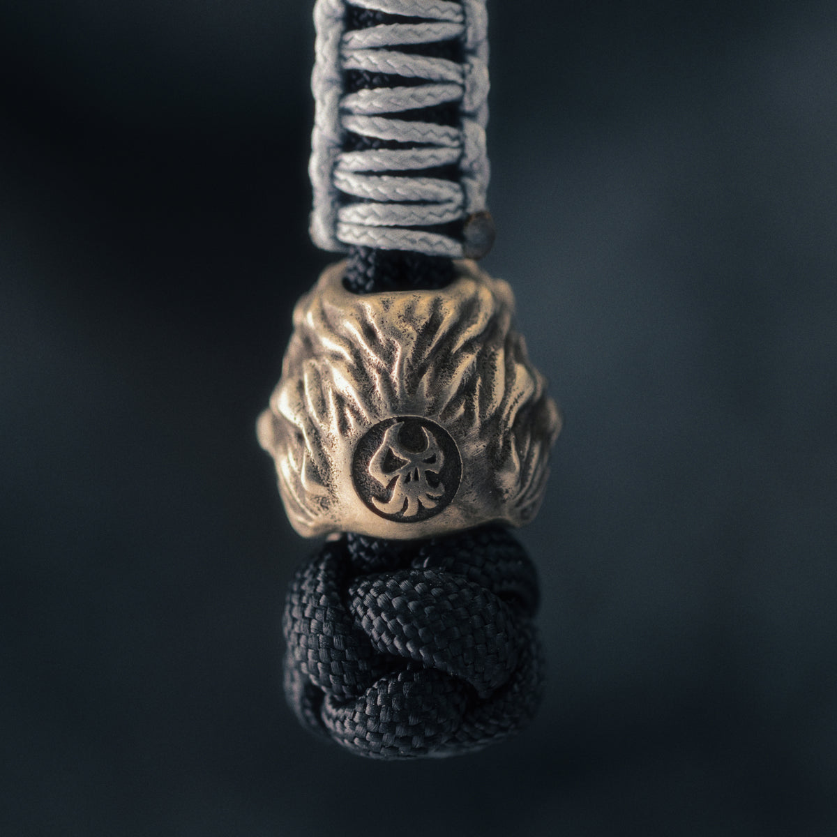 Rear view of a ShadowEDC lion paracord bead showing the sculpted mane, hand-aged metal surface and maker’s mark.