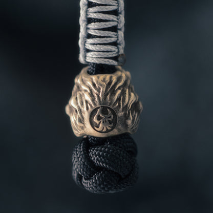 Rear view of a ShadowEDC lion paracord bead showing the sculpted mane, hand-aged metal surface and maker’s mark.
