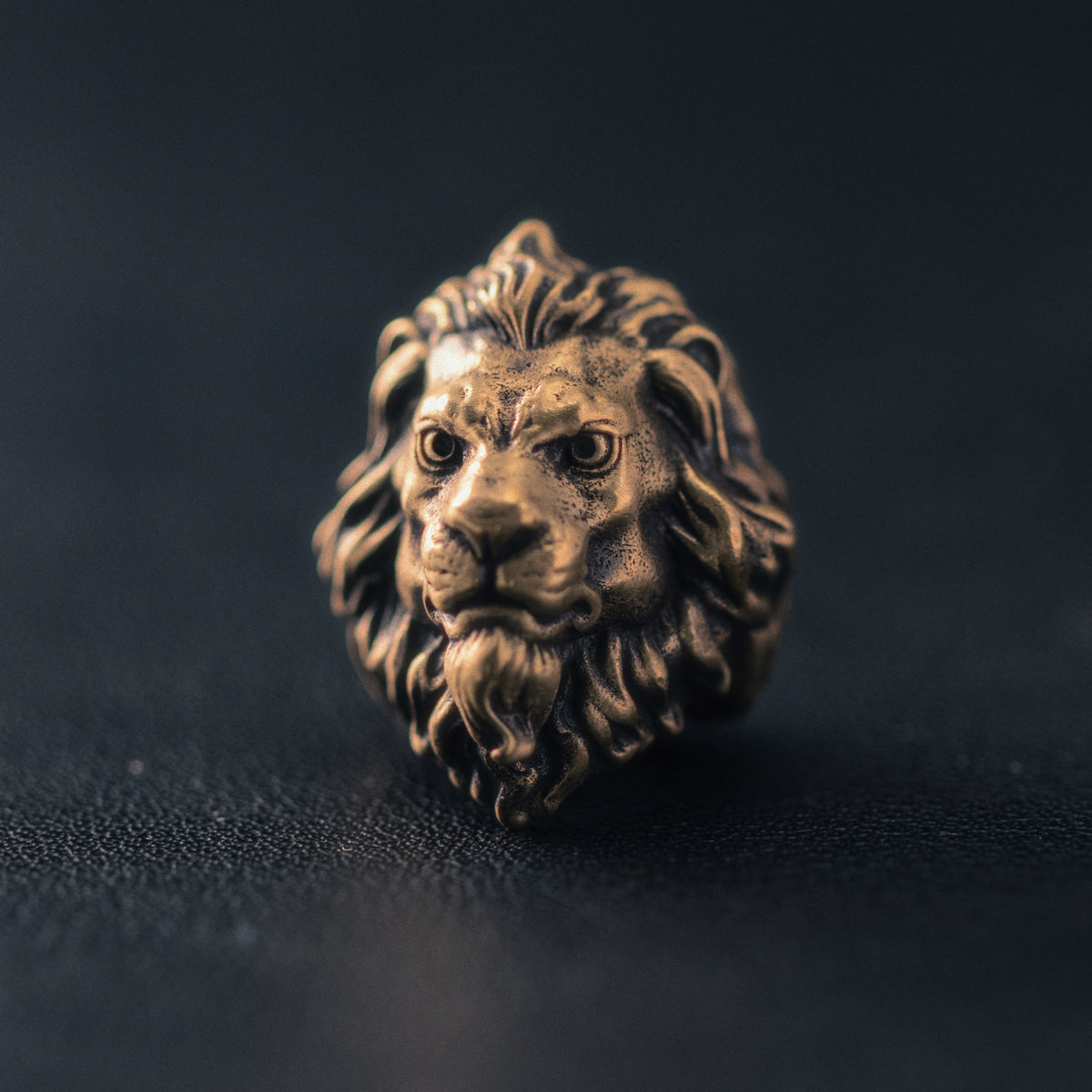 Front view of a sculpted lion EDC bead with deep-set eyes, strong muzzle and flowing mane in an antique brass finish.