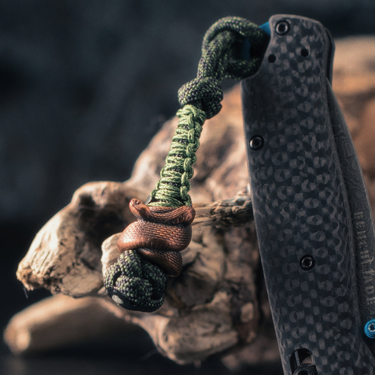 Rattlesnake paracord bead on a green knife lanyard beside an EDC folding knife, designed for standard 550 paracord.