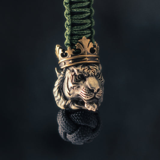 Side view of a crowned tiger paracord bead highlighting the detailed muzzle, layered fur, engraved stripes and aged brass crown.