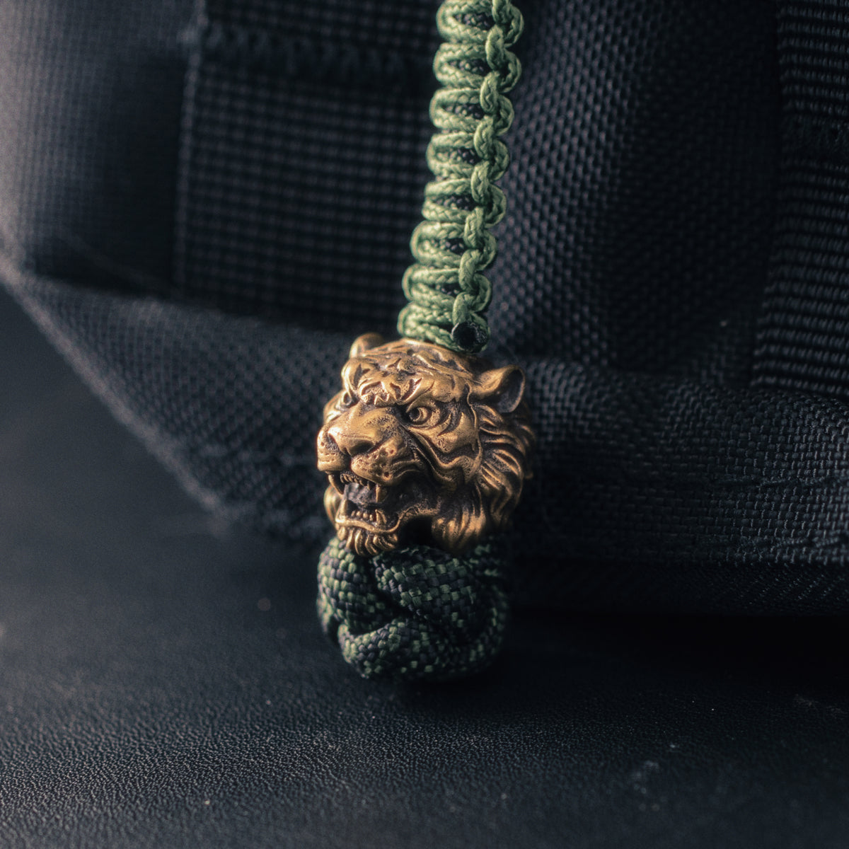 Three-quarter view of a brass tiger head paracord bead showing exposed fangs, carved facial stripes and hand-aged metal finish.